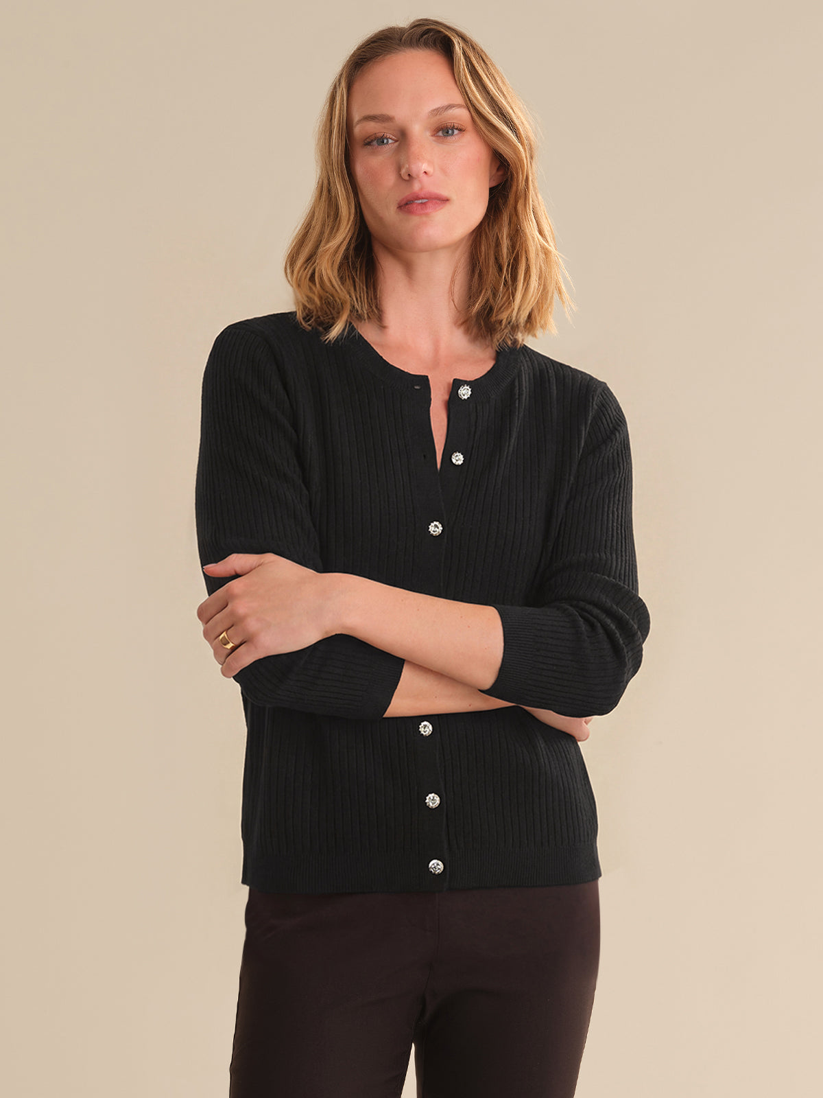 Woman wearing a black ribbed sweater with button details on a beige background
