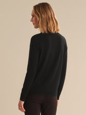 Person wearing a black sweater against a beige background