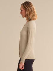 Woman wearing a beige ribbed sweater against a plain background