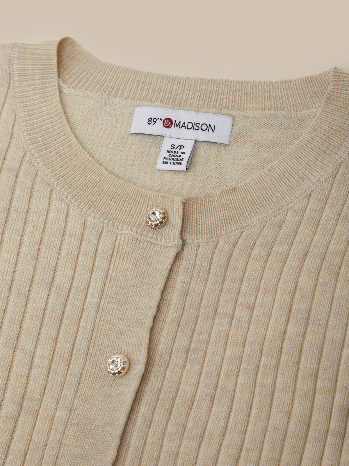 Close-up of a beige ribbed sweater with a brand label on a beige background
