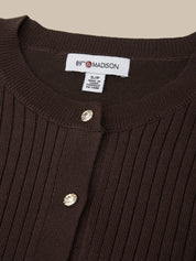 Close-up of a brown ribbed sweater with buttons and a visible label on a beige background