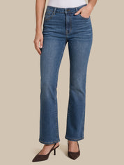 A model wearing a pair of medium-wash blue denim jeans with a straight-to-flare leg, paired with dark brown pointed-toe heels against a solid beige background.