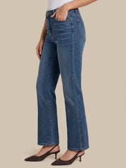 A model wearing a pair of medium-wash blue denim jeans with a straight-leg or bootcut fit, styled with dark brown slingback heels against a solid beige background.