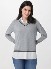 Woman wearing a gray sweater over a white shirt with blue jeans on a light gray background