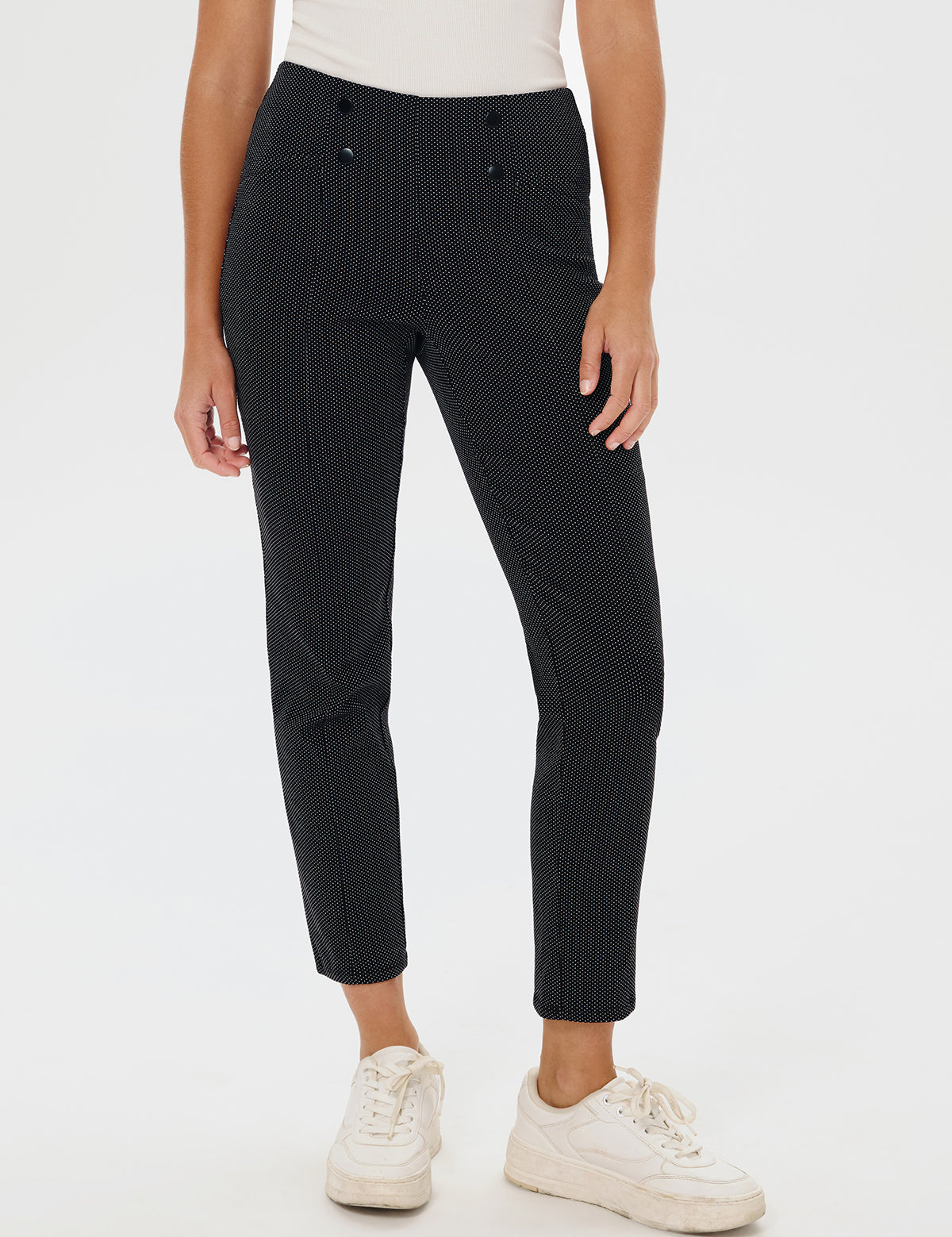 Person wearing black patterned pants and white sneakers on a white background