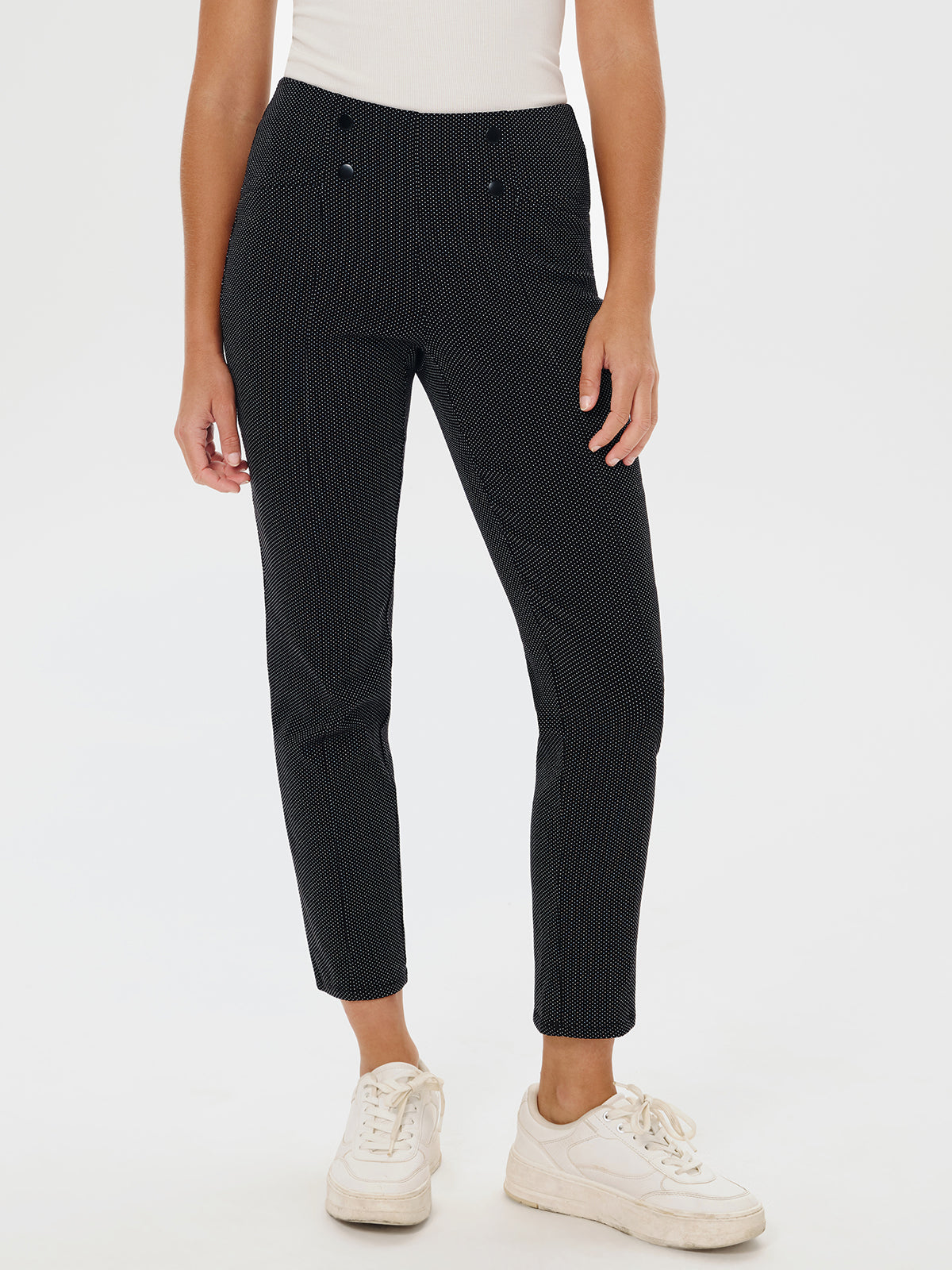 Person wearing black patterned pants and white sneakers on a white background