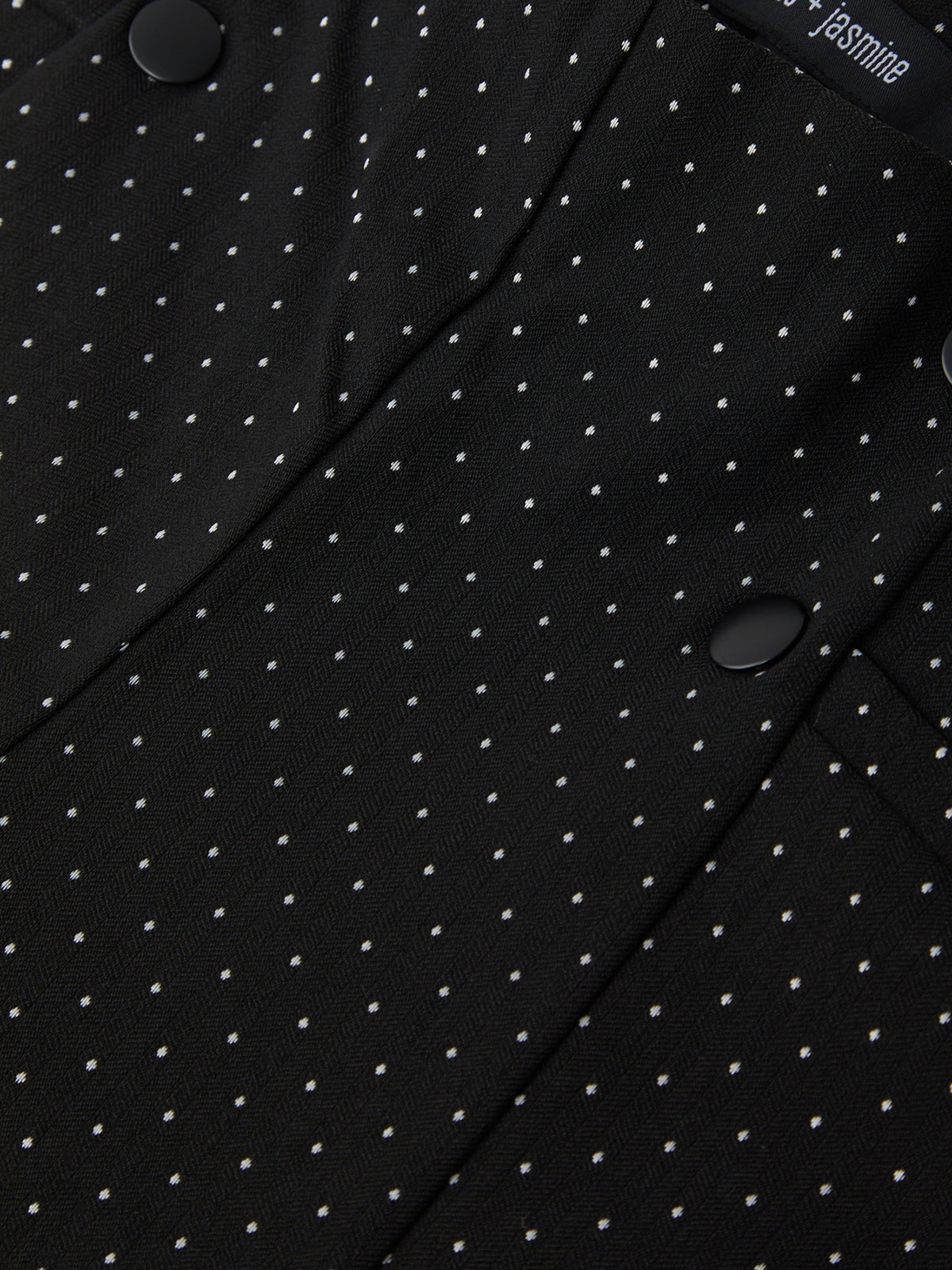 Close-up of a black fabric with white polka dots and a brand label.
