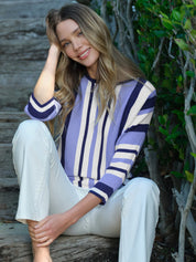Woman wearing a striped sweater and white pants sitting outdoors.