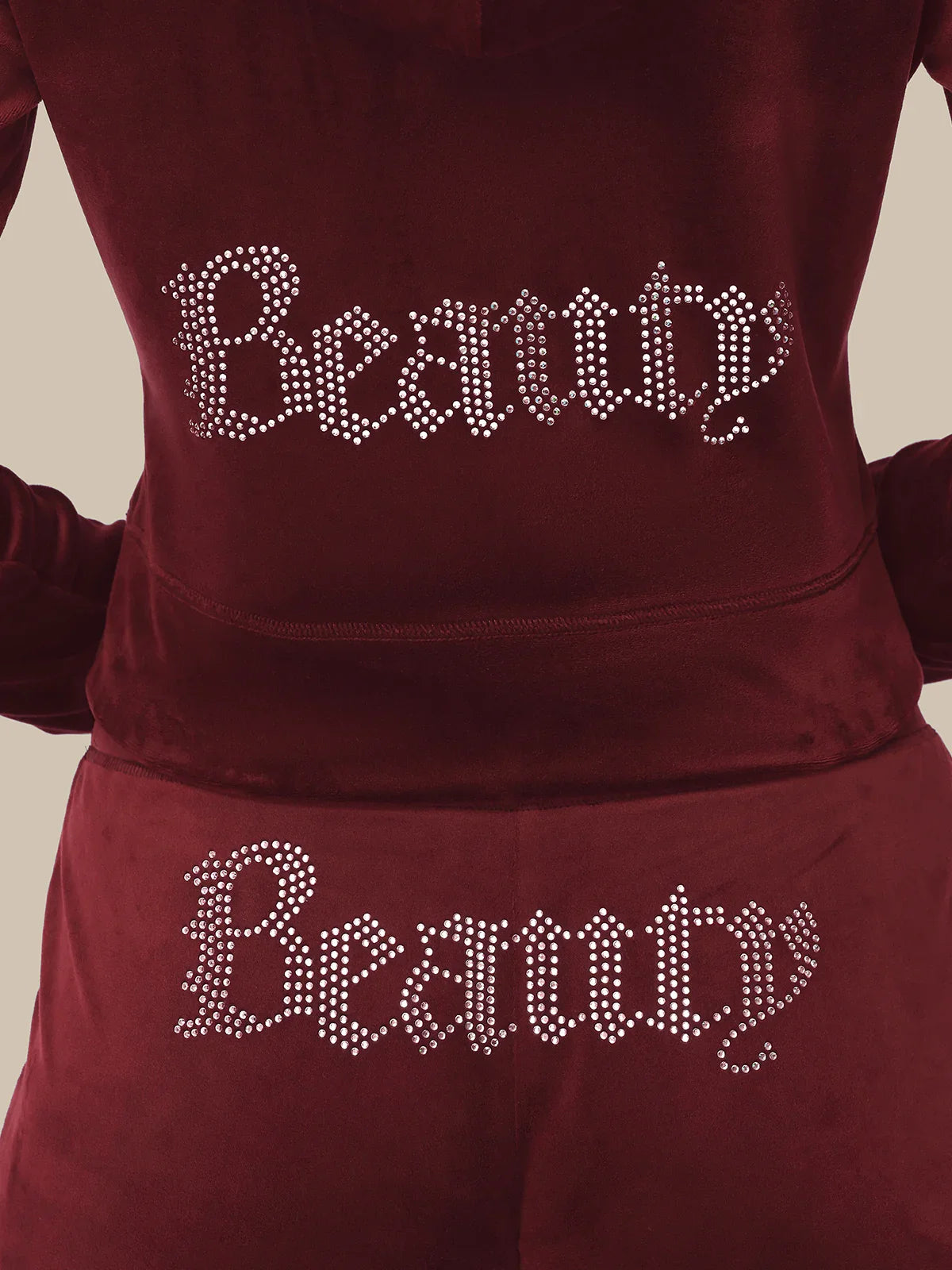 Maroon hoodie with 'Beauty' text in rhinestones on a beige background