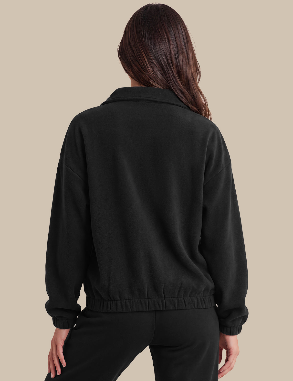 A woman shown from the back wearing a black cropped jacket with a wide collar and elasticated hem, paired with black pants, against a solid beige background.