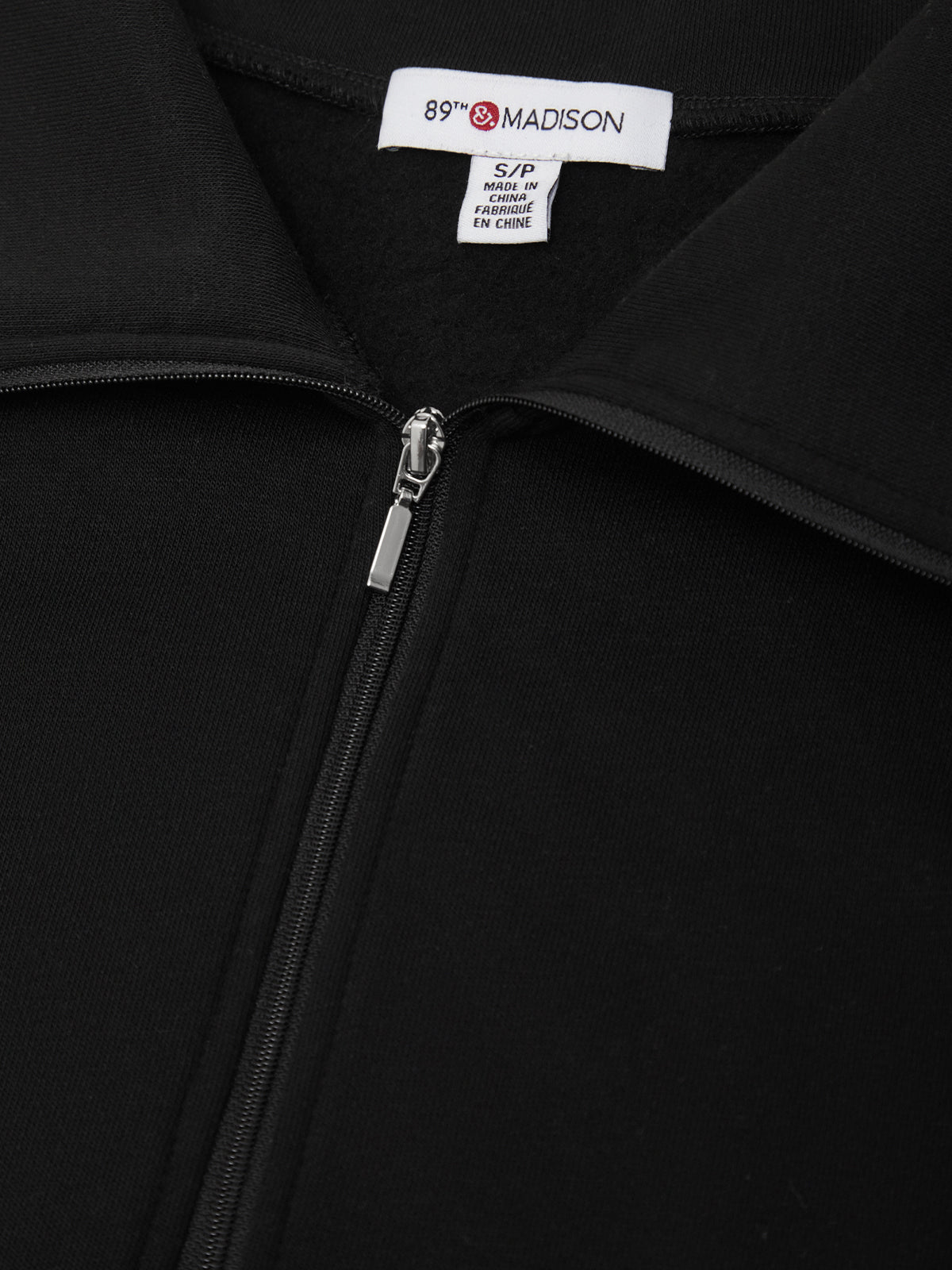 Close-up of a black zip-up jacket collar with a white interior neck label reading 89th & MADISON.