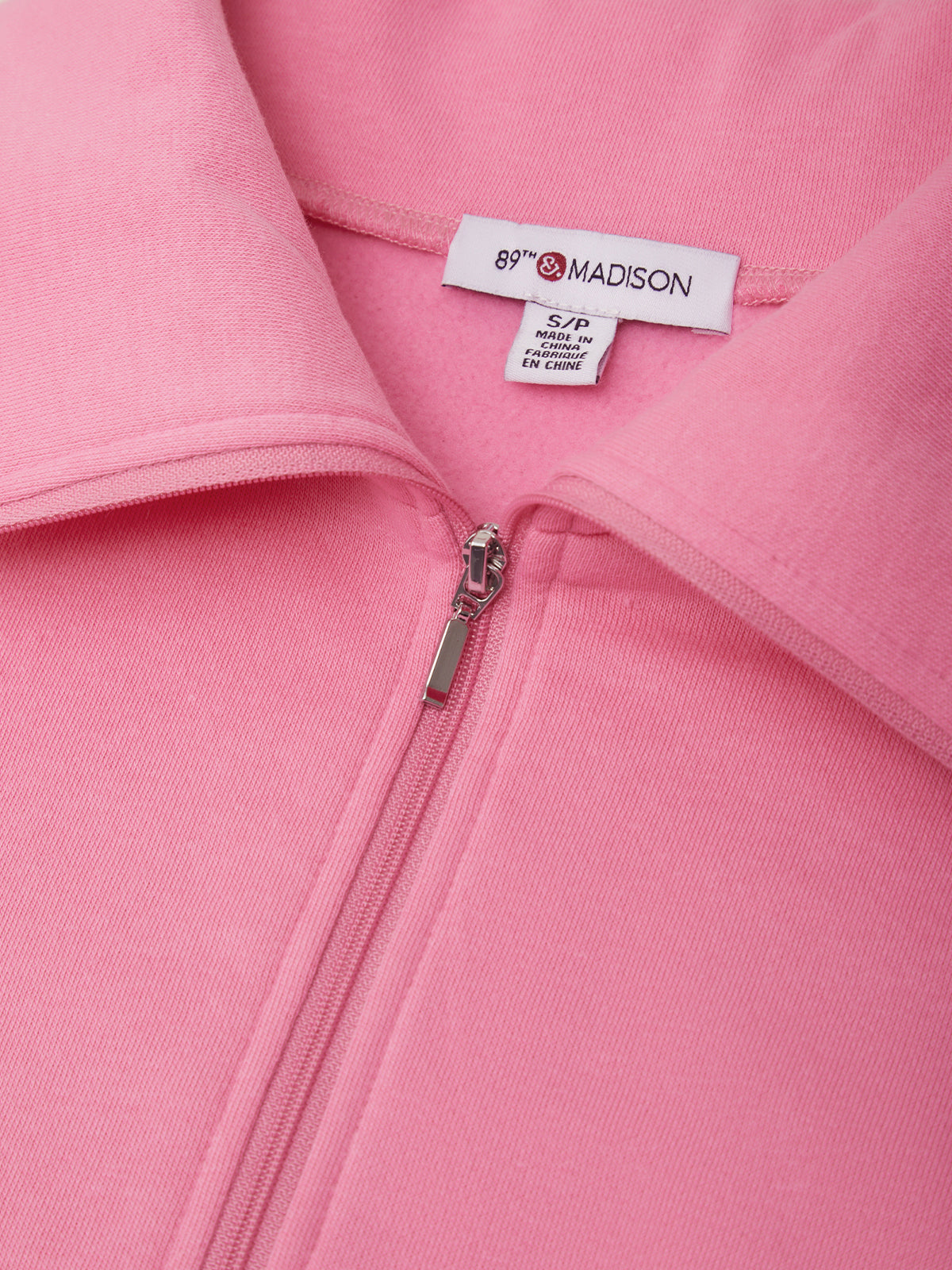 Close-up of a pink zip-up jacket with a collar, showing a white interior neck label that reads 89th & MADISON.