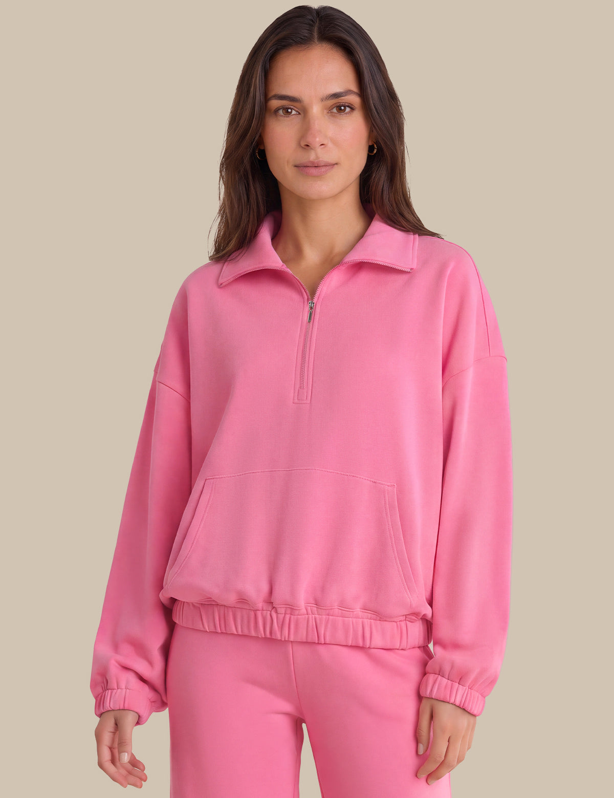 A woman modeling a bright pink half-zip sweatshirt and matching sweatpants against a solid beige background.