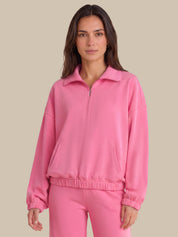 A woman modeling a bright pink half-zip sweatshirt and matching sweatpants against a solid beige background.