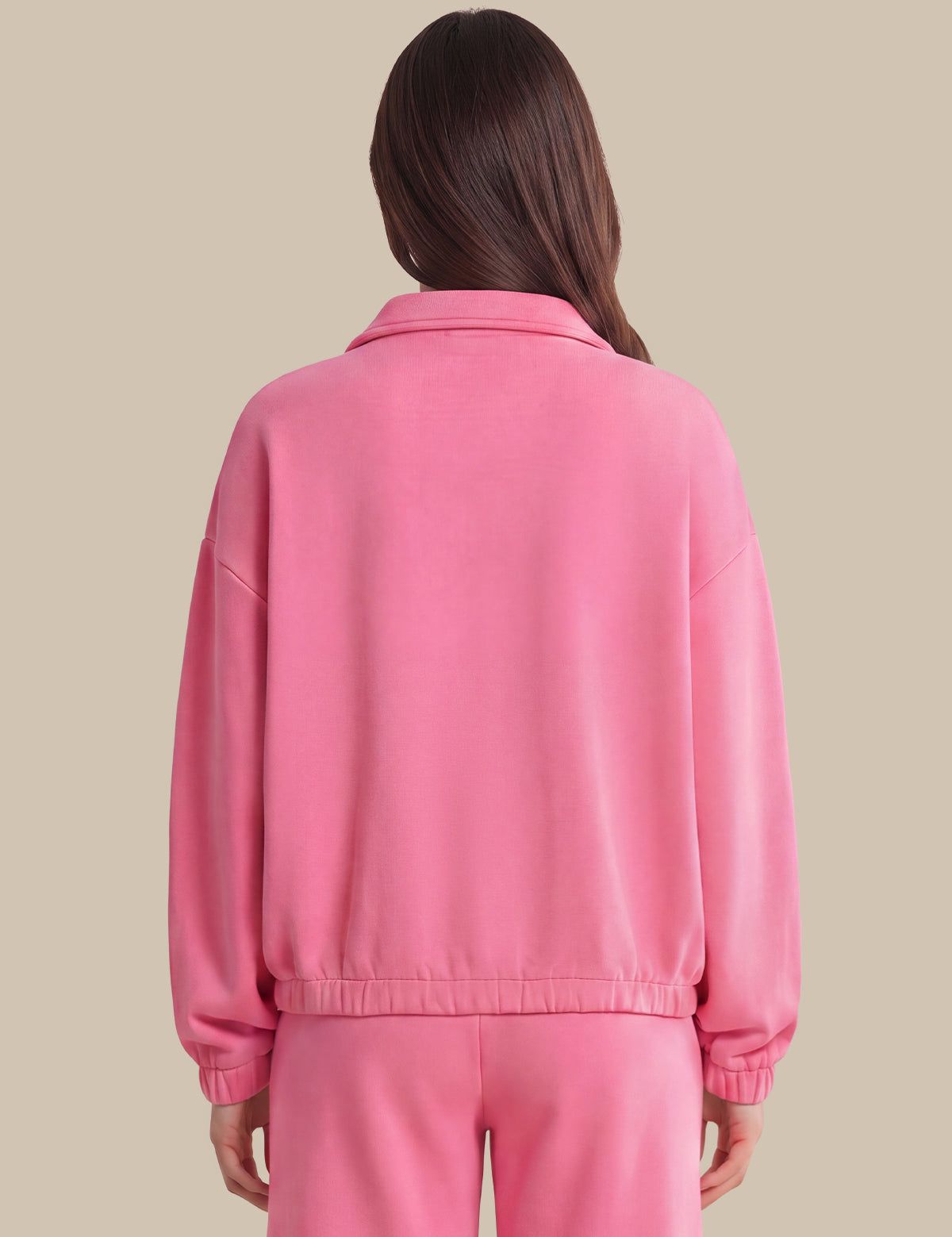 A woman viewed from the back wearing a pink cropped jacket and matching pink pants against a solid beige background.