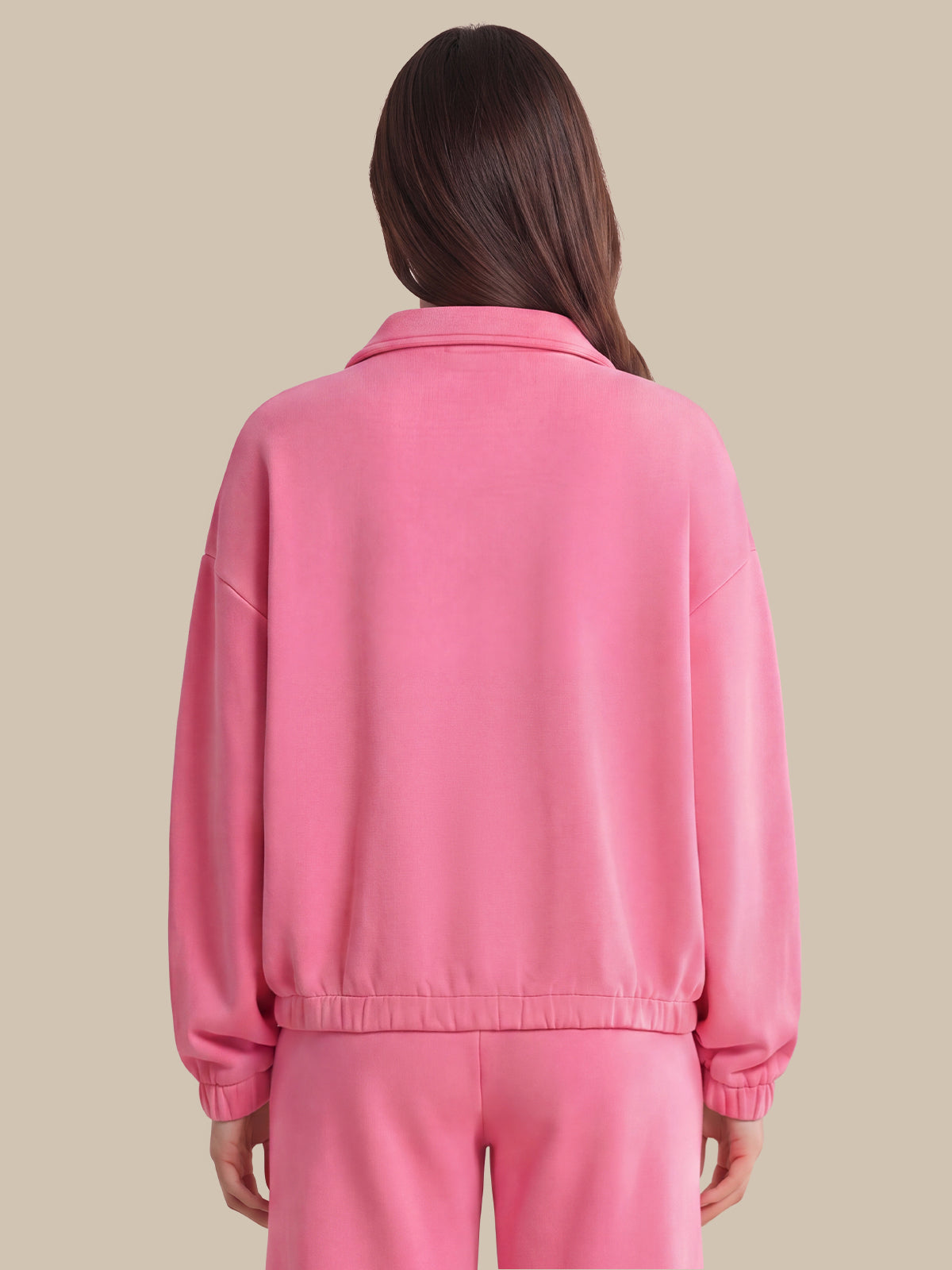 A woman viewed from the back wearing a pink cropped jacket and matching pink pants against a solid beige background.