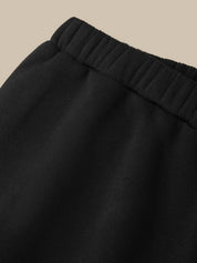 Close-up of a black fabric garment showing a ribbed elastic waistband against a plain beige background.