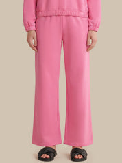 A person wearing bright pink wide-leg sweatpants with a matching top and black slide sandals, shown from the chest down against a plain beige studio background.