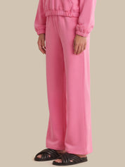 A person wearing a matching pink lounge set with wide-leg sweatpants and a cropped long-sleeve top, paired with black slide sandals, against a plain beige studio background.