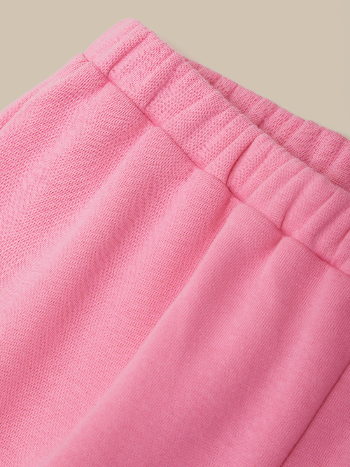 Close-up of pink knit fabric with an elasticized waistband, shown against a plain warm beige background.