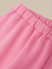 Close-up of pink knit fabric with an elasticized waistband, shown against a plain warm beige background.