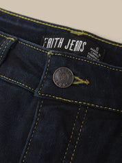 Close-up of dark indigo denim jeans showing the waistband, yellow contrast stitching, a round metal button, and a visible Faith Jeans brand label.