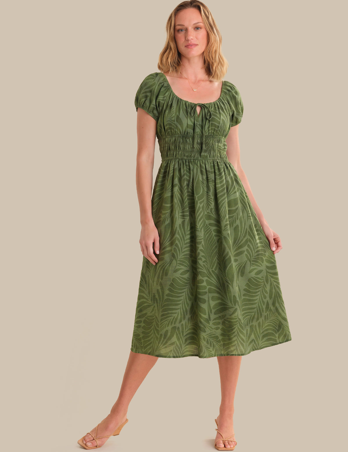 Woman wearing a green dress with leaf pattern on a beige background