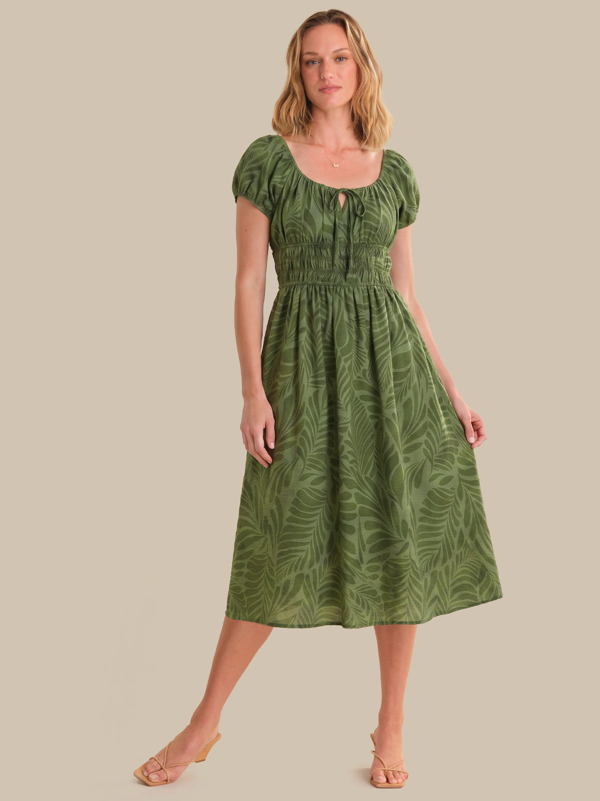 Woman wearing a green dress with leaf pattern on a beige background