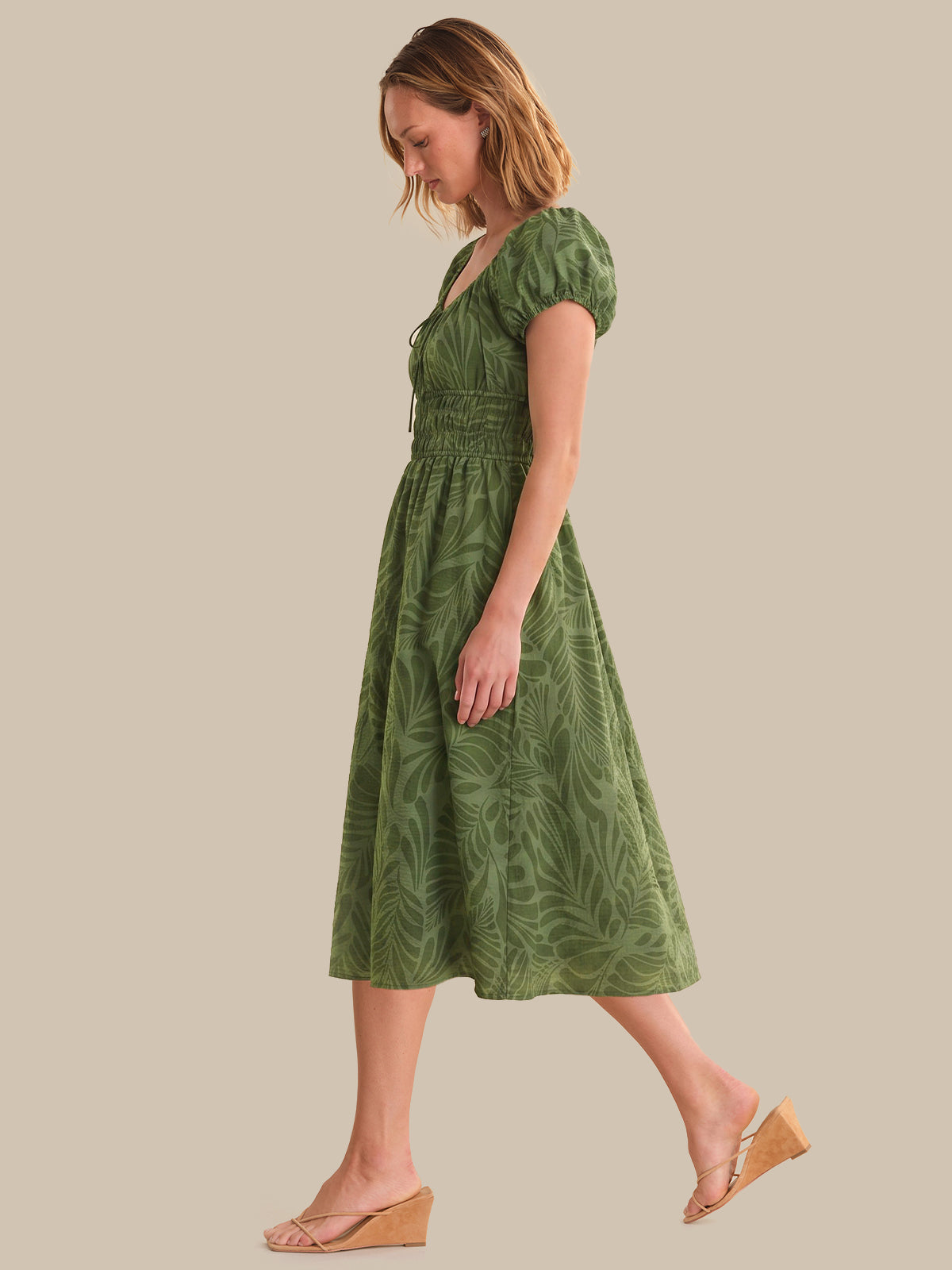 Woman wearing a green dress with leaf pattern on a beige background