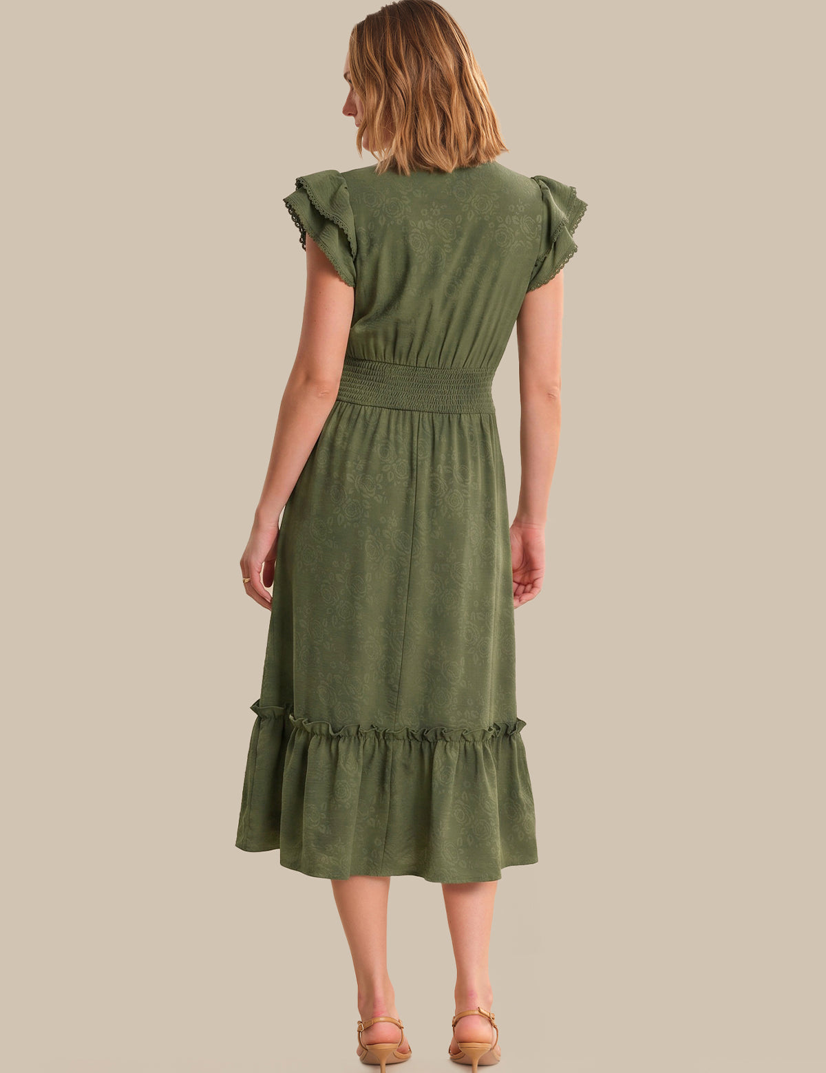 Woman wearing a green dress with ruffled sleeves and hem on a beige background