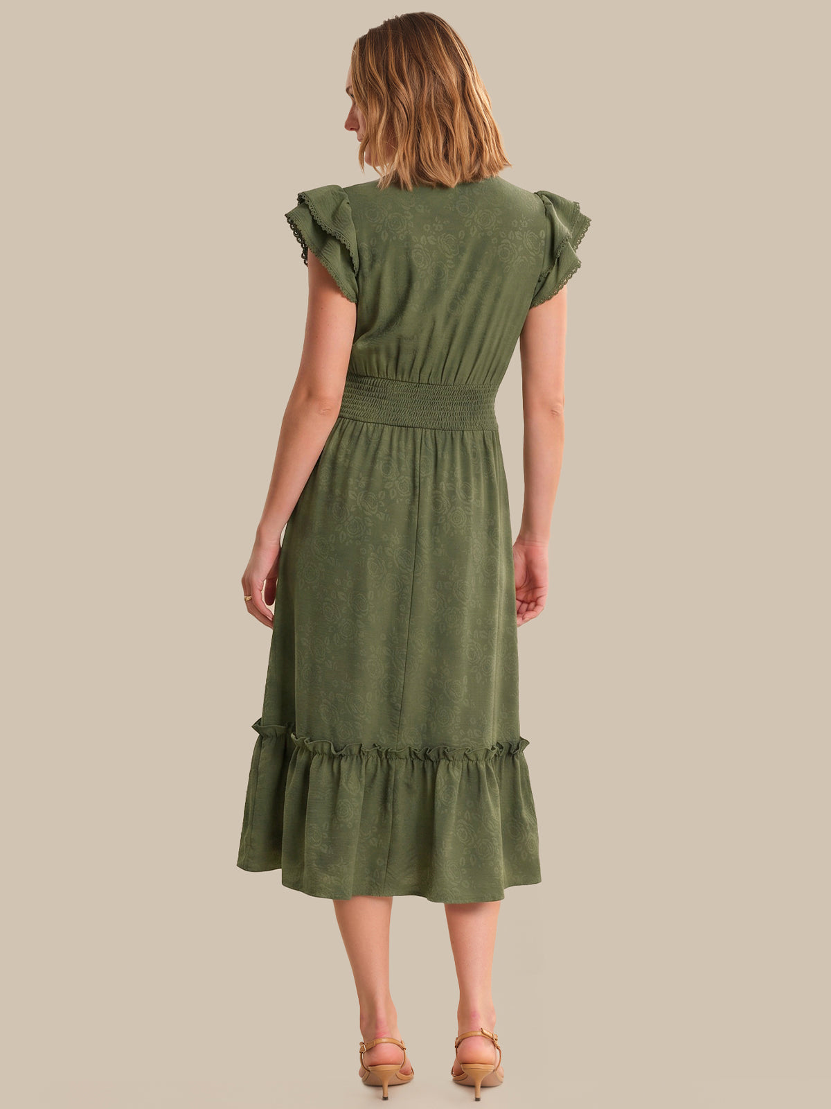 Woman wearing a green dress with ruffled sleeves and hem on a beige background