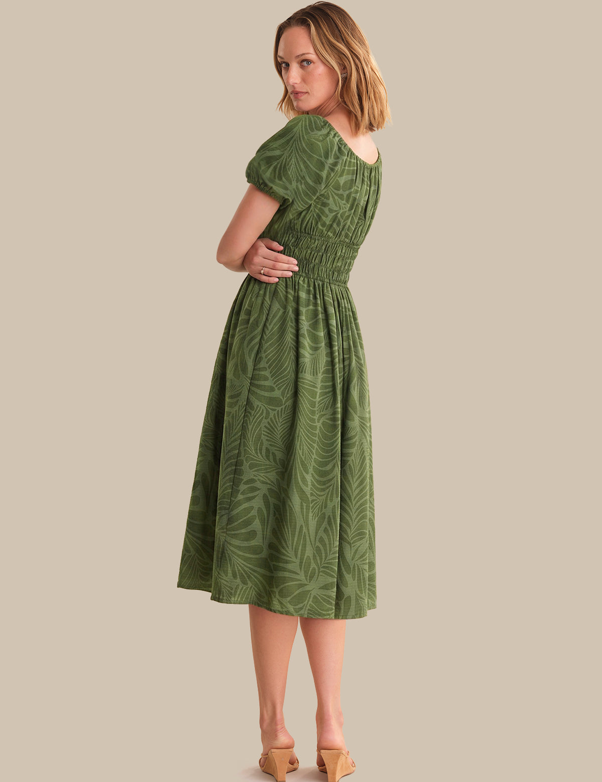Woman wearing a green dress with a leaf pattern on a beige background