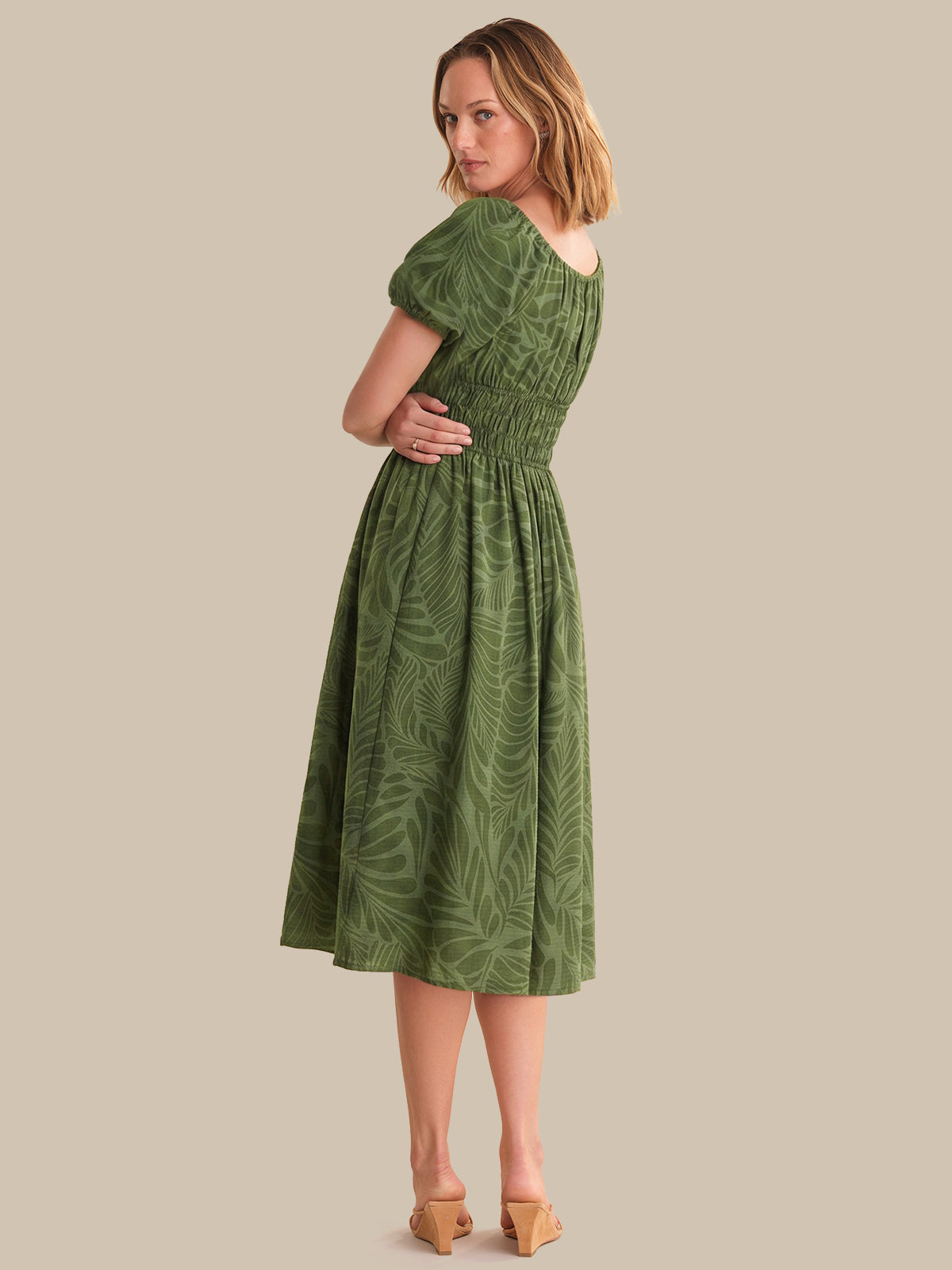 Woman wearing a green dress with a leaf pattern on a beige background