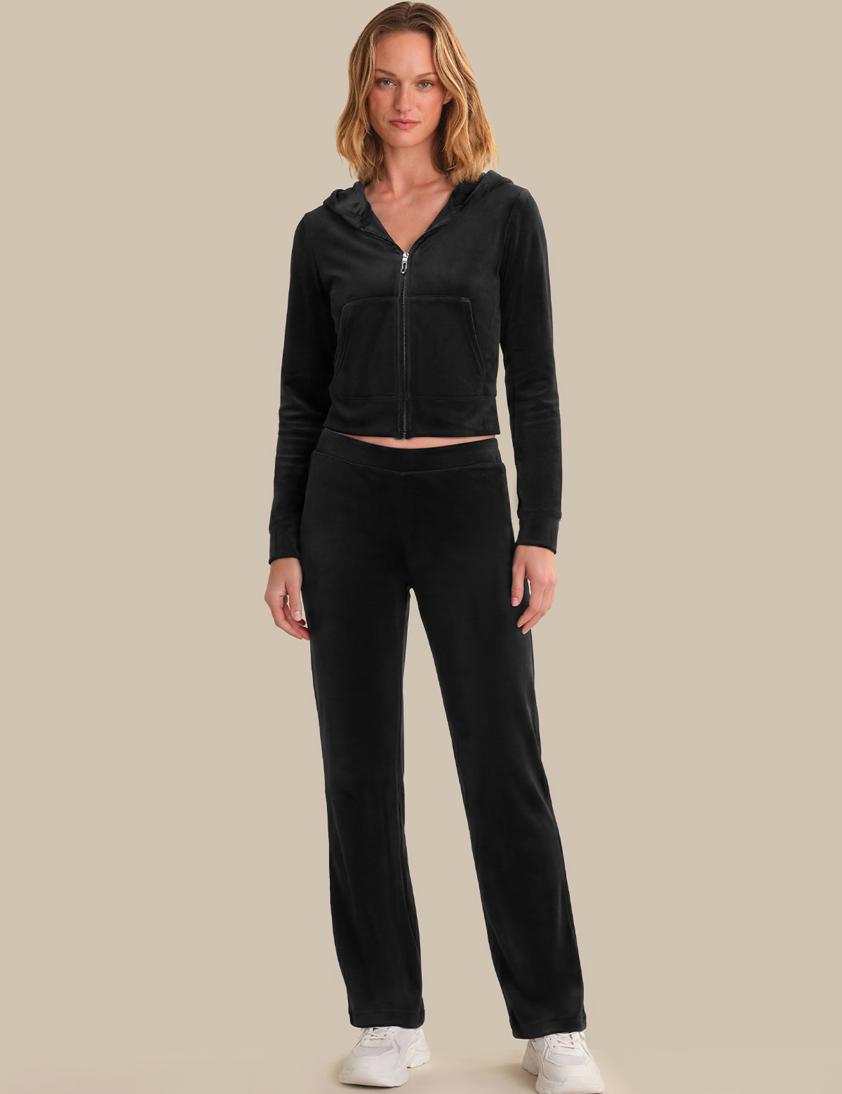 Woman wearing a black hoodie and pants on a beige background