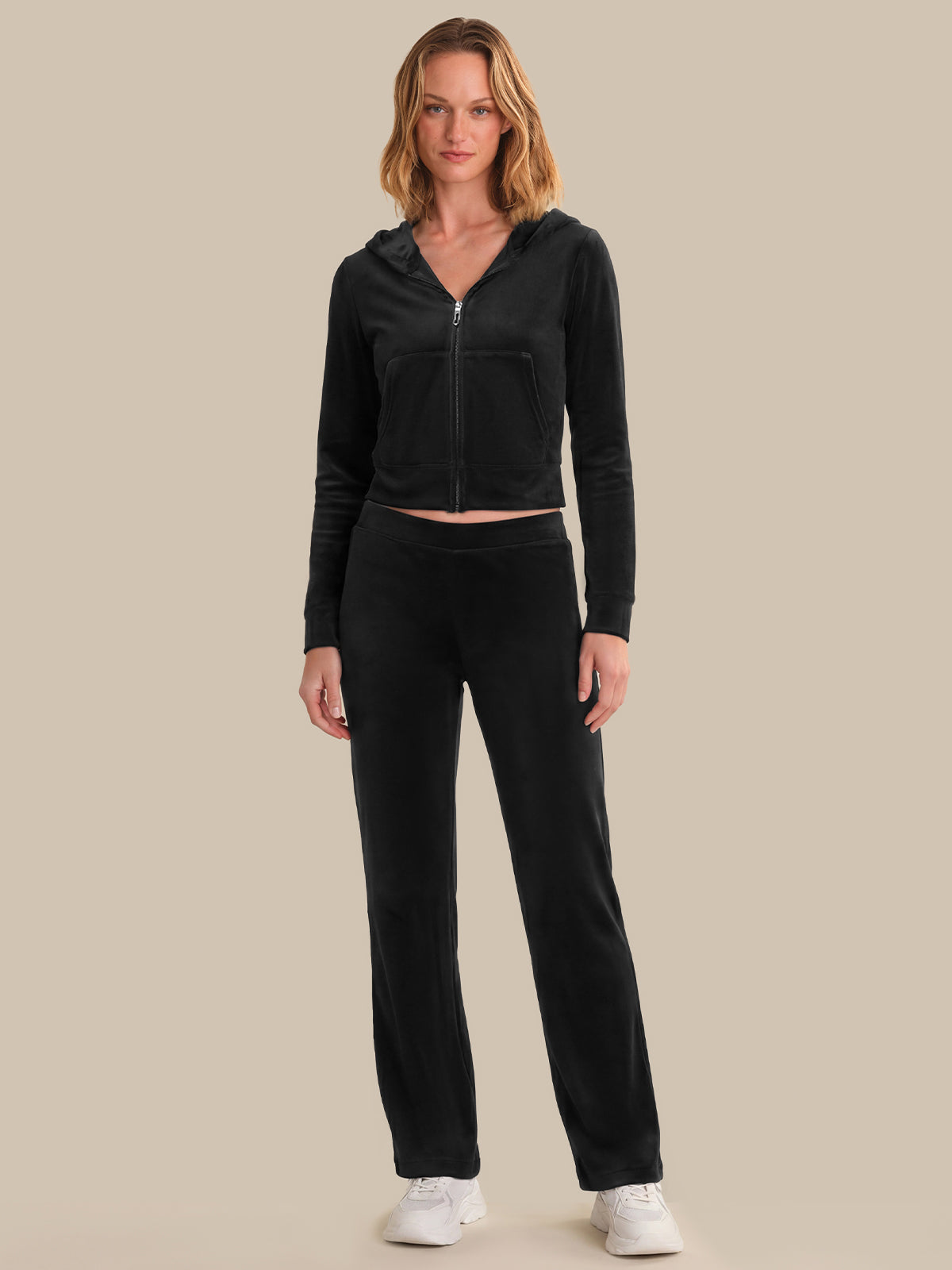 Woman wearing a black hoodie and pants on a beige background