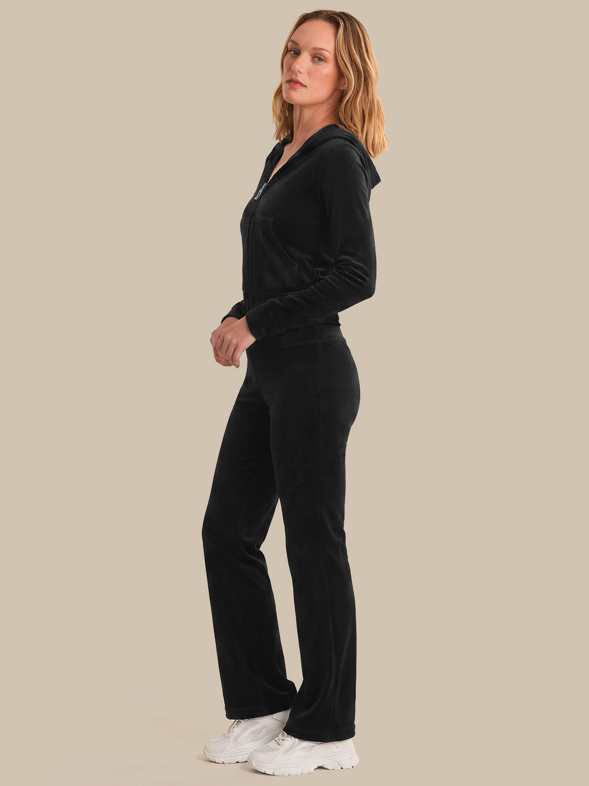 Woman wearing a black velvet tracksuit on a beige background