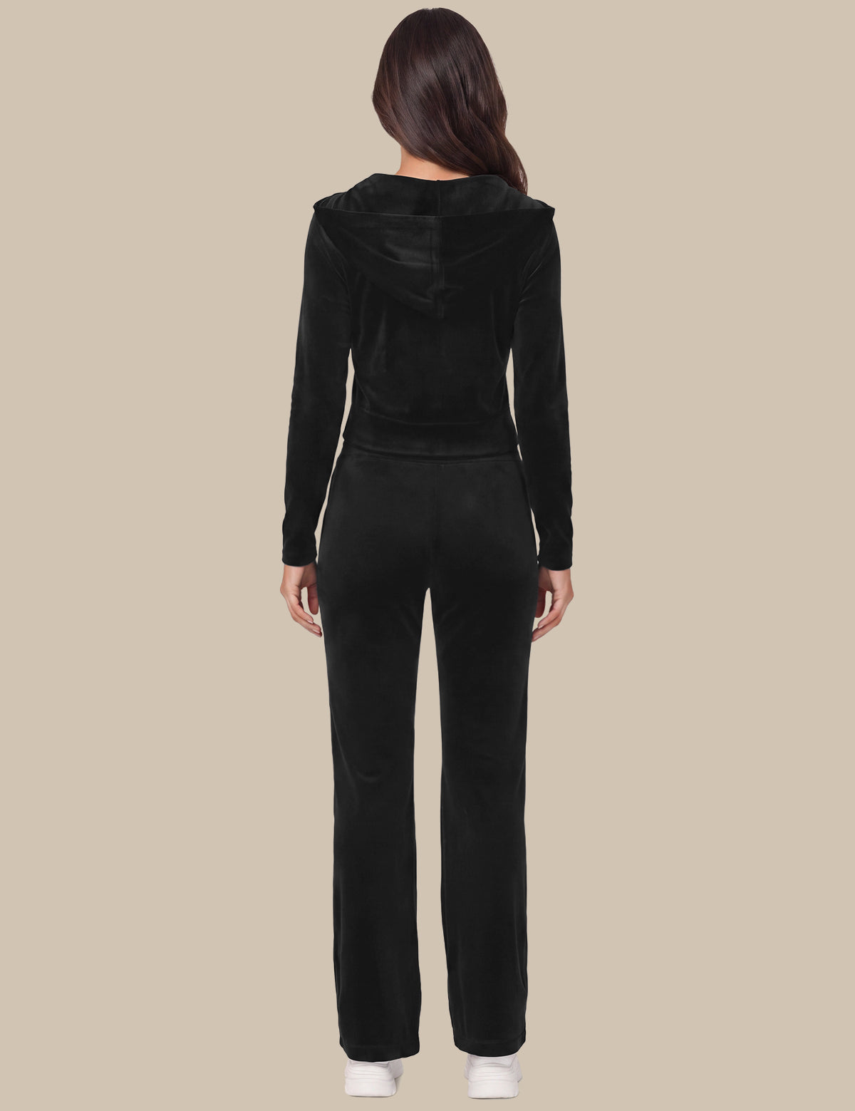 A woman viewed from the back wearing a black long-sleeve cropped hoodie and matching black pants against a plain beige studio background.