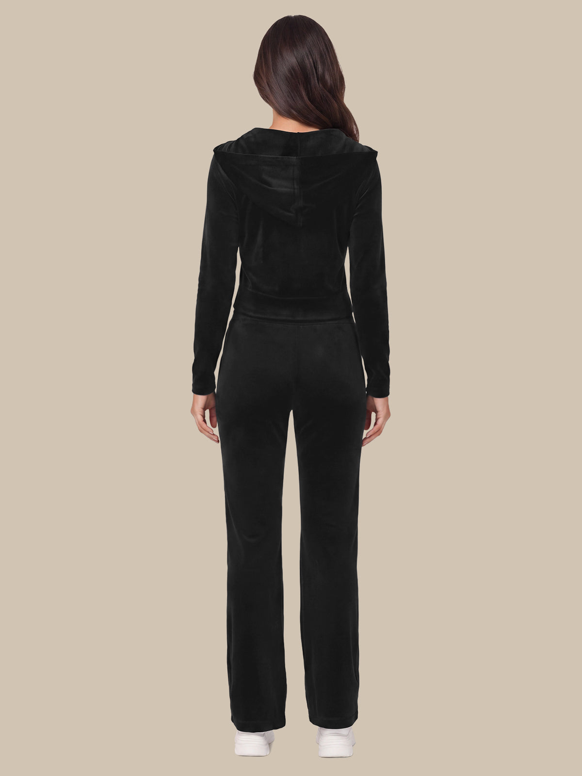 A woman viewed from the back wearing a black long-sleeve cropped hoodie and matching black pants against a plain beige studio background.