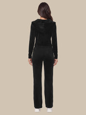 A woman viewed from the back wearing a black long-sleeve cropped hoodie and matching black pants against a plain beige studio background.