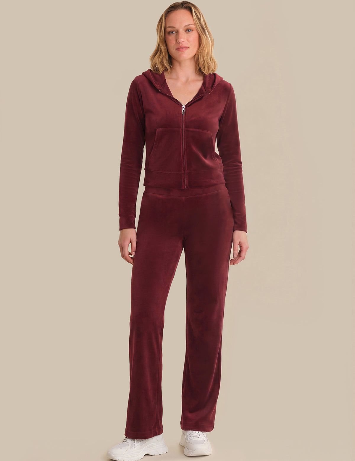 Woman wearing a burgundy tracksuit against a beige background