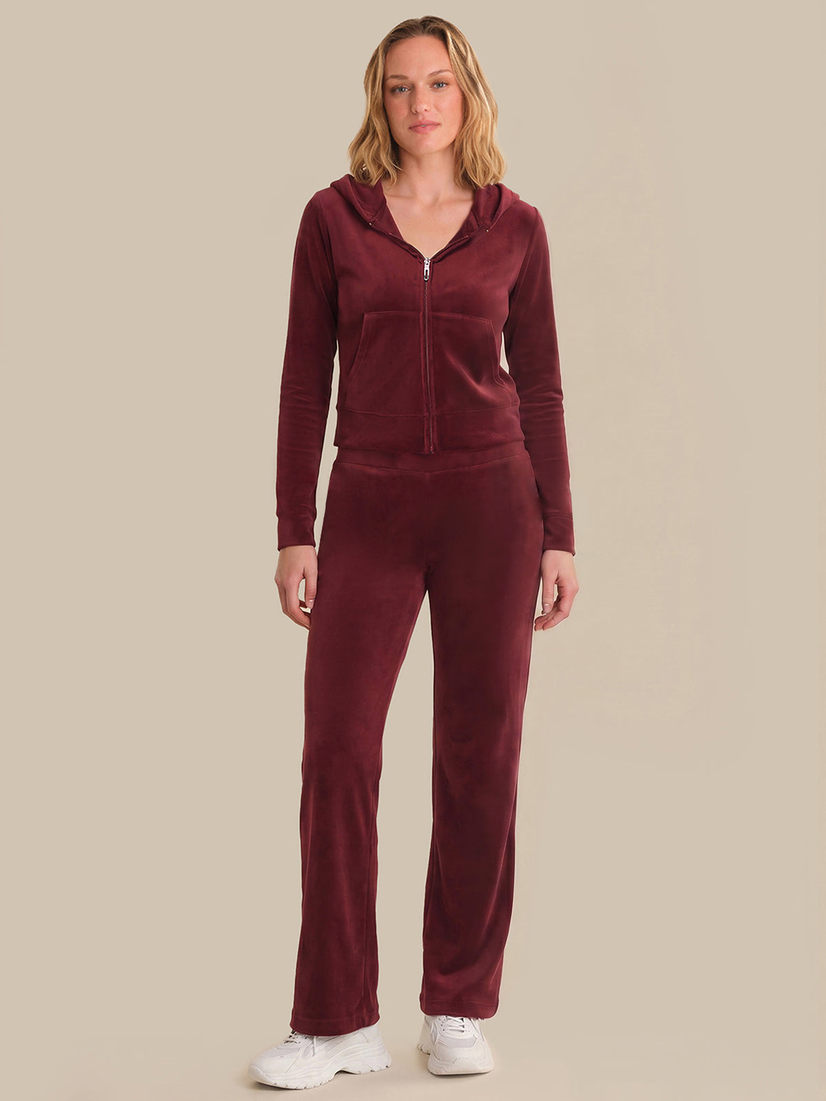 Woman wearing a burgundy tracksuit against a beige background