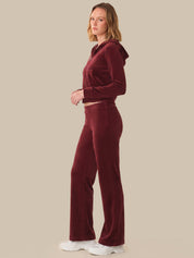 Woman wearing a burgundy velvet tracksuit on a beige background
