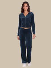 A woman modeling a matching dark navy blue velour loungewear set, consisting of a cropped zip-up hoodie and matching pants, against a solid beige background.