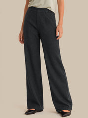 A model wearing dark charcoal gray wide-leg trousers, paired with a light beige top and black pointed flats, against a solid beige background.