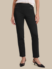A model wearing black ankle-length straight-leg trousers, styled with a white knit top and black pointed-toe kitten heels, set against a solid beige background.