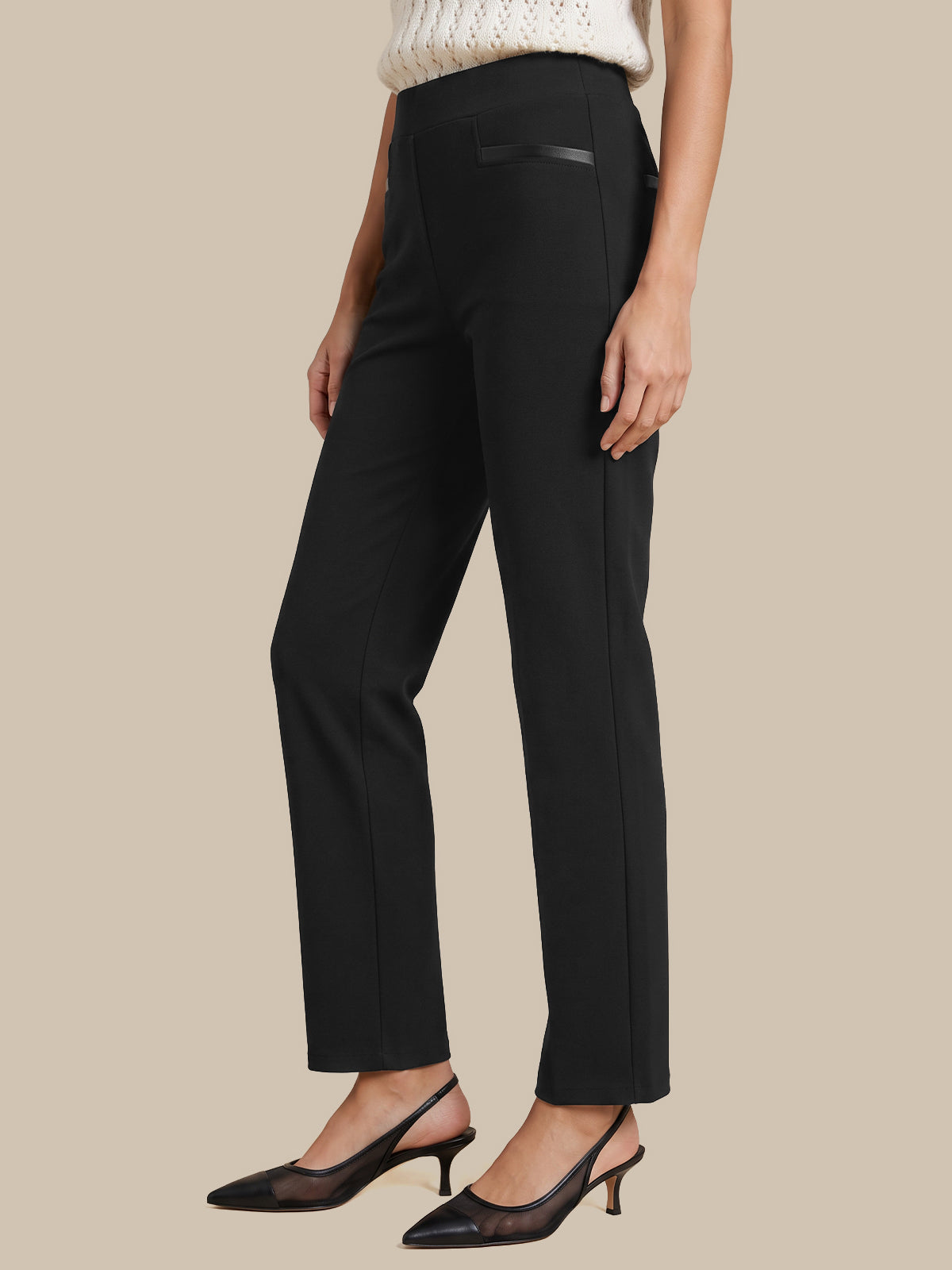 A model wearing black high-waisted straight-leg trousers with a subtle black leather detail on the front pocket, styled with a cream knit top and black slingback heels against a solid beige background.