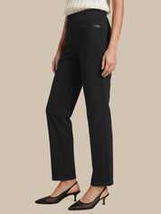 A model wearing black high-waisted straight-leg trousers with a subtle black leather detail on the front pocket, styled with a cream knit top and black slingback heels against a solid beige background.