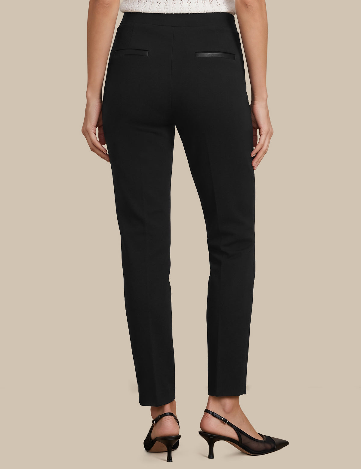 Rear view of a model wearing black slim-fit trousers with small welt back pockets, paired with black slingback heels against a solid beige background.