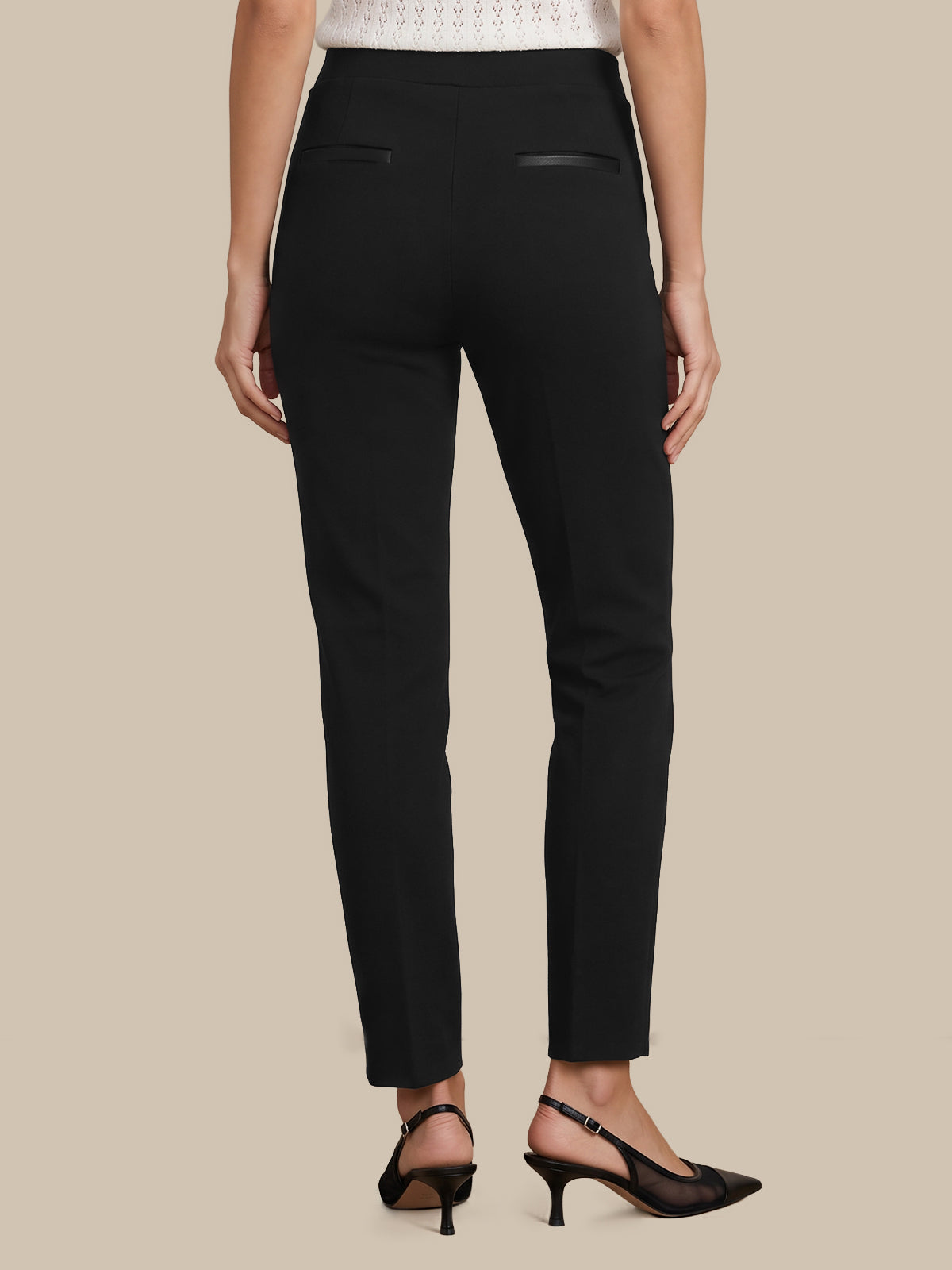 Rear view of a model wearing black slim-fit trousers with small welt back pockets, paired with black slingback heels against a solid beige background.
