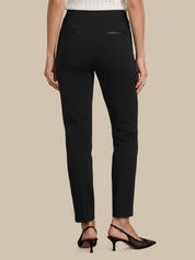Rear view of a model wearing black slim-fit trousers with small welt back pockets, paired with black slingback heels against a solid beige background.